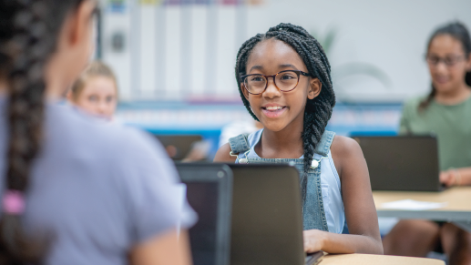 A student wearing glasses looks up from her laptop at her desk. 