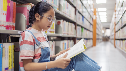 Investing with Agency: A child sits against a shelf of books reading.