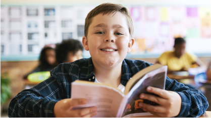 Reading with Excitement: A child looks up from his book smiling.